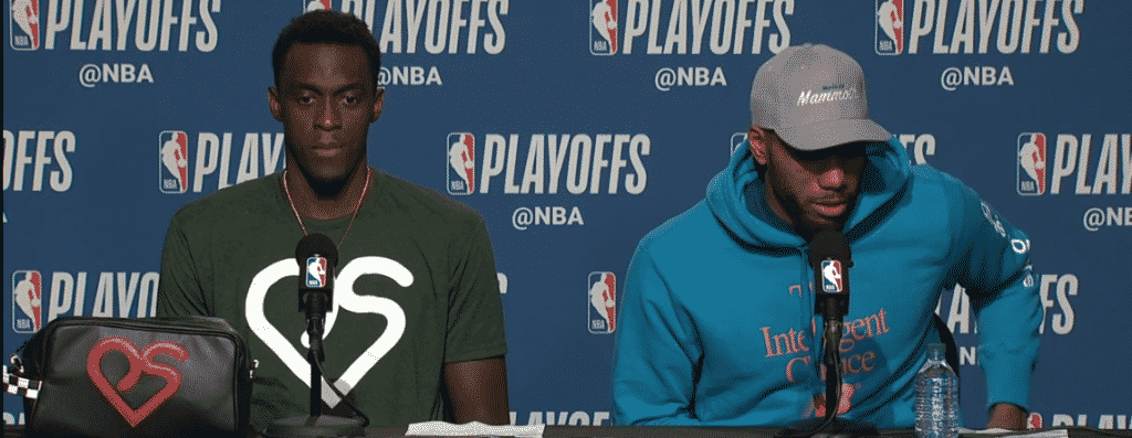 Pascal Siakam wearing a green t-shirt with a white version of his personal logo during a press conference.