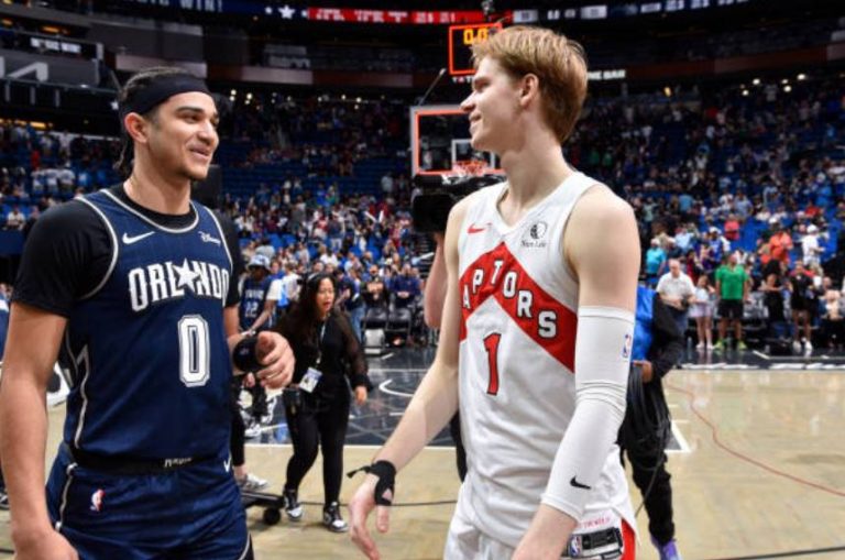 Gradey Dick and Anthony Black smiling courtside in Orlando Magic and Toronto Raptors jerseys.