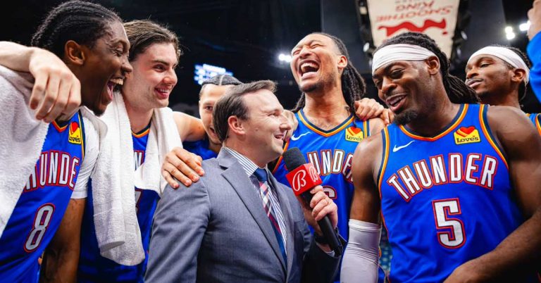 Nick Gallo holds a microphone among Oklahoma City Thunder players wearing blue uniforms.