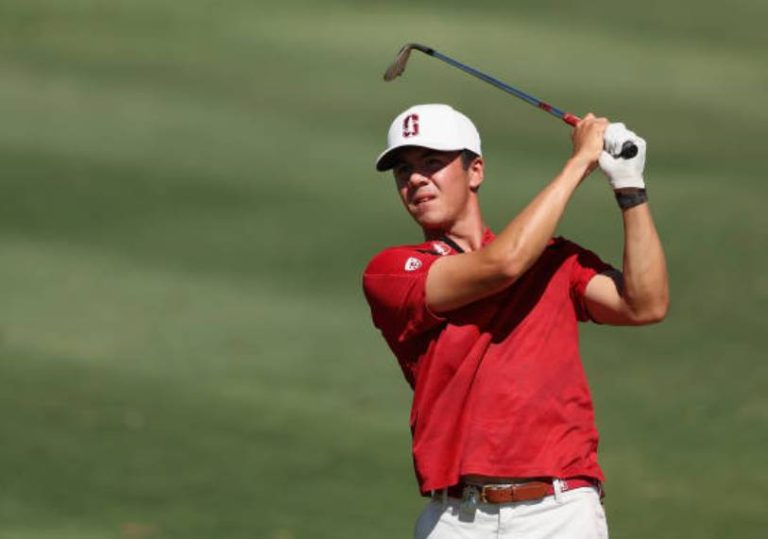 College golfer in a red shirt and white cap follows through on a golf swing.