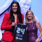 Two women hold a Chicago basketball jersey numbered 24 in front of a WNBA-themed display.