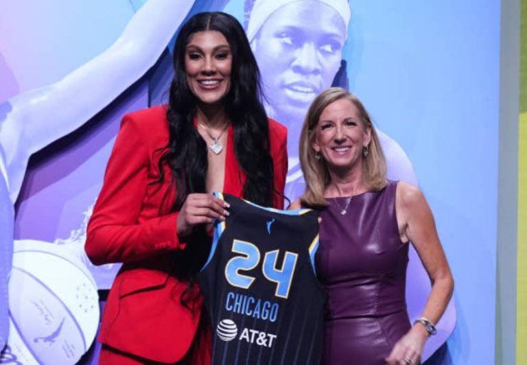 Two women hold a Chicago basketball jersey numbered 24 in front of a WNBA-themed display.