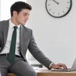 Business professional holding a soccer ball while working on a laptop in an office